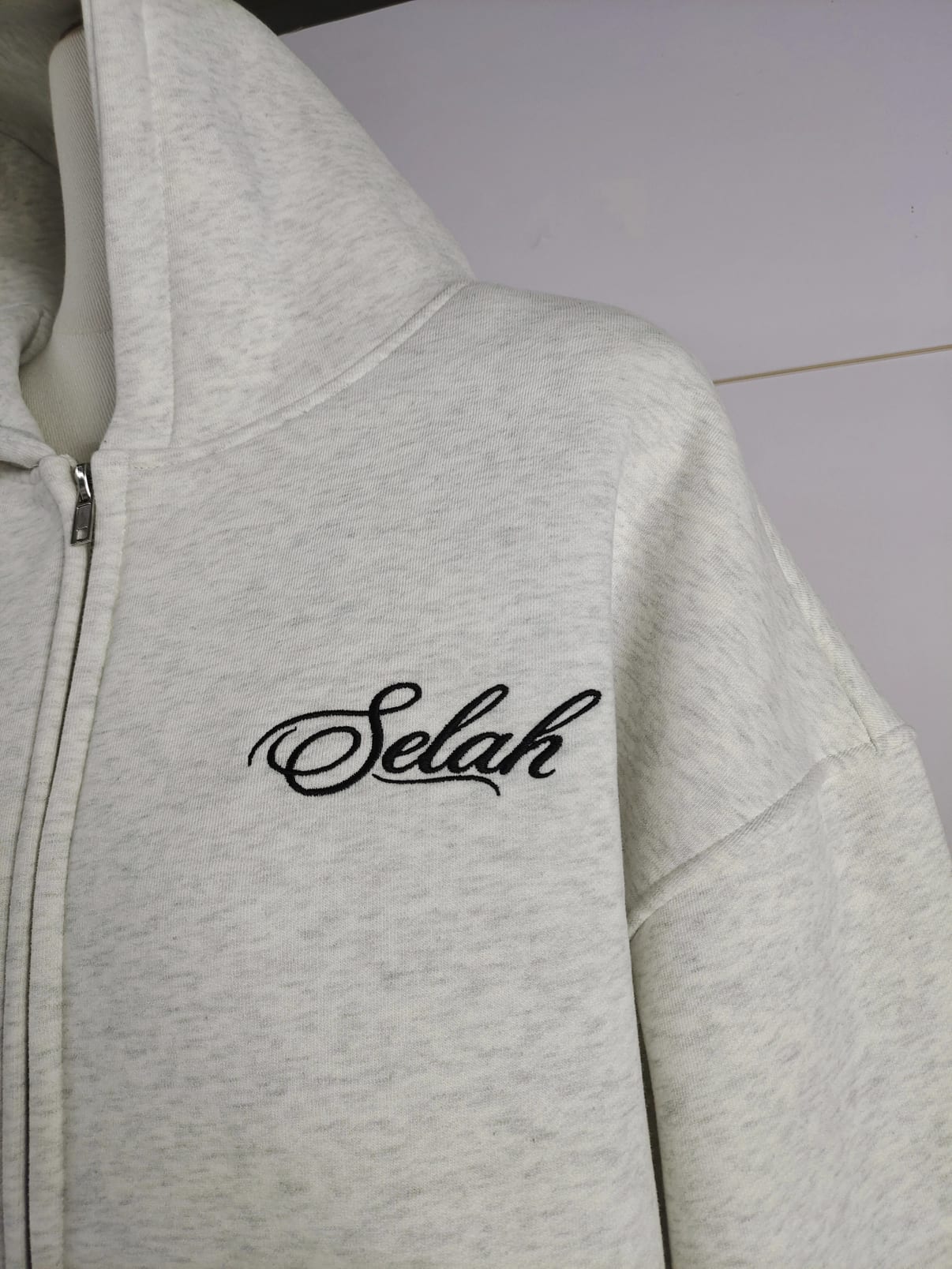 Chest detail of the washed bone hoodie with black Selah embroidery